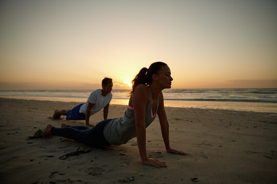Fitness, sunset and yoga with couple on beach together for holistic health or wellness routine. Balance, exercise and summer with people outdoor on sand by ocean for awareness or mindfulness
