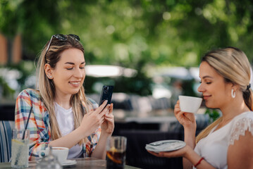 Two young women enjoying coffee and using smartphone at outdoor cafe