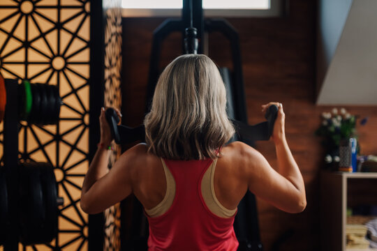 Determined senior woman performing lat pulldown exercise in home gym