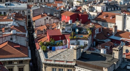 Dense cluster of old building rooftops with red tiles, chimneys, and satellite dishes creating a chaotic urban pattern in a historic European city on a sunny day