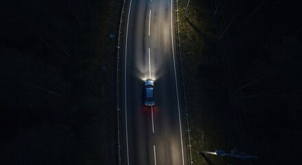 Modern blue sedan car driving alone on a dark rural highway at night, with bright headlights illuminating the empty asphalt road, captured from a top-down aerial perspective