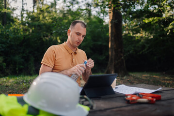 Obraz premium Surveyor opening water bottle while working with tablet in park