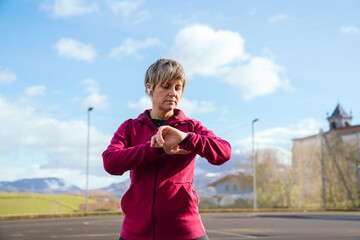 Woman standing outdoors, looking at her fitness tracking device, monitoring workout progress and health data