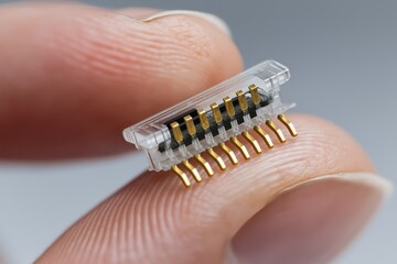 Macro close-up of a tiny electronic connector held between fingers, showcasing gold pins and plastic housing