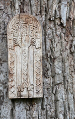 Wooden Armenian khachkar with traditional carvings mounted on a tree trunk in a forest