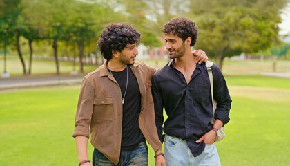 Indian happy young adult gen z smart boy guys pair standing talk gossip share new plan enjoy day. Happy cool male man pair mate speak funny joke humor have fun joy spend break time place garden park