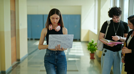 Indian young gen z busy woman lady hold laptop in hand look screen check new email notes walk campus place. Teen girl female use device do exam study online e learning work skill data day time