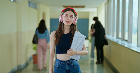 Indian young adult gen z lady student wear headphone enjoy mp3 music hold laptop in hand walk indoor campus place Asian happy girl use headset listen new song have fun joy spend day break time inside