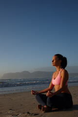 Fototapeta premium Woman, meditation and fitness for yoga on ocean with mindfulness, spiritual healing and zen. Person, lotus pose and space with holistic balance, inner peace and mental health for self care at beach