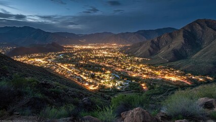 Desert valley city at night, glowing streetlights winding through the valley between rugged mountain ranges. Concept Desert Nightscape, Valley City Lights, Winding Streetlights