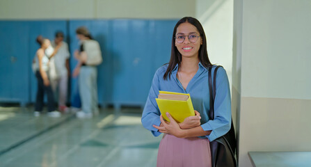 Indian young adult gen z pupil smart girl wear glass cross arm hold book in hand ready for exam campus place. Happy pretty lady female staring look cam do casual pose enjoy new good day time