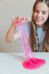 Girl lifting and stretching a thick, glossy stream of vibrant pink slime. Fun sensory toy and trendy DIY activity