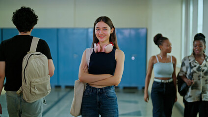 Indian young adult gen z female lady confident student standing hold bag pack fold hand look camera indoor campus place happy smiling girl cross arms staring cam do casual pose enjoy new college