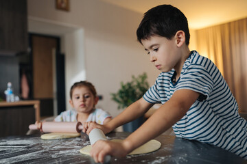 Fototapeta premium young boy carefully concentrates on baking alongside his brother or sister in tranquil kitchen atmosphere