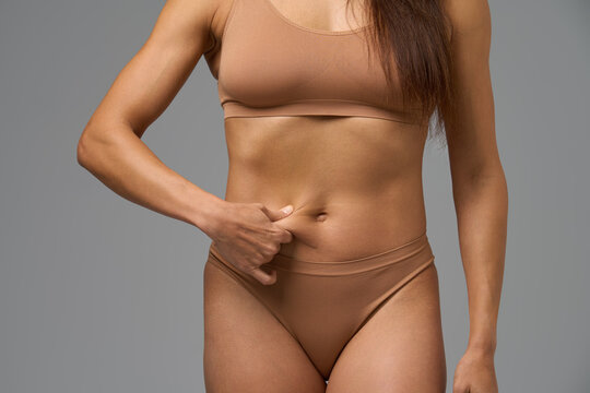 Fit woman in beige underwear pinching her belly skin showing body composition