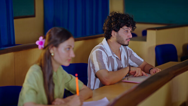 Indian young adult gen z busy pupil boy girl guys sitting on desk table hold pencil do study work exam notes class room. Smart male man female learn new task project day time inside college place