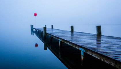 Red balloon tied to a wooden pier on a foggy, tranquil lake