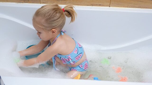 Little child girl in a swimsuit bathing in a bubble bath