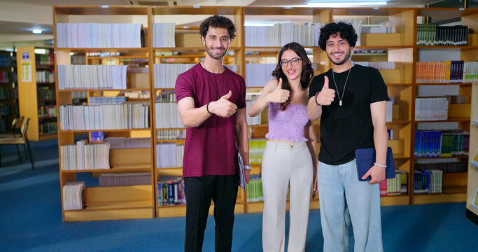 Indian happy young adult gen z male man group standing indoor library look camera spend break time Asian boy girl great team show thumbs up hand sign staring cam do casual pose enjoy fun joy day