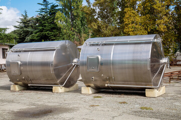 Shiny steel wine production tanks lying on the asphalt on a clear sunny day. Winemaking viticulture wine blend.