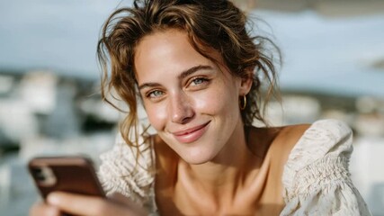 Smiling woman enjoying time outdoors while using her phone on a sunny day by the water
