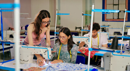 Indian young adult gen z woman lady wear tape around neck talk learn new clothe craft sewing course. Teen pupil girl female sitting desk help to stitch teach casual skill day indoor class room place