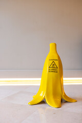 A bright yellow banana sculpture stands upright on a smooth surface. The background is minimalistic with soft lighting, emphasizing the playful design. © Alina