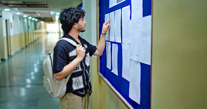 Indian young adult gen z busy boy guy look notice board check study exam results report campus area Teen man male wear bag do read new paper list name data project date time day at college place
