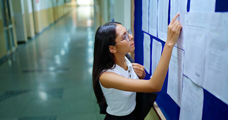 Indian young adult gen z busy pupil girl look notice board check study exam results report campus...