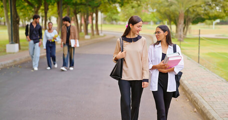 Indian happy young adult gen z lady female walk wear glass talk gossip share new day plan enjoy break time outdoor place. Teen pupil girl guys hold book speak funny joke have fun joy park