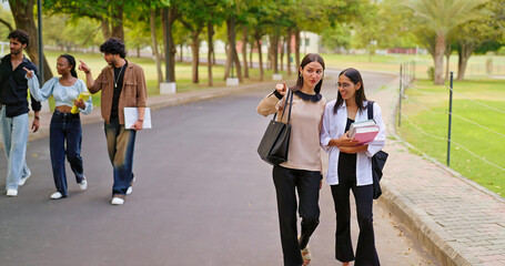 Indian happy young adult gen z lady female walk wear glass talk gossip share new day plan enjoy break time outdoor place. Teen pupil girl guys hold book speak funny joke have fun joy park