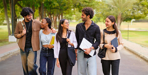 Obraz premium Indian happy young adult gen z walk female male man guys talk gossip share new day plan enjoy break time outdoor place. Happy pupil teen age girl boy group speak funny have fun joy park