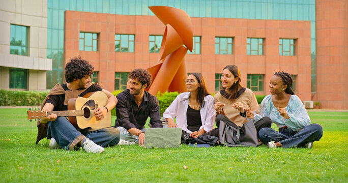 Indian young adult gen z male man group hold guitar play music lady woman group sing new song sitting garden park Happy relax girl boy team guy spend break time mood have fun joy enjoy good day place