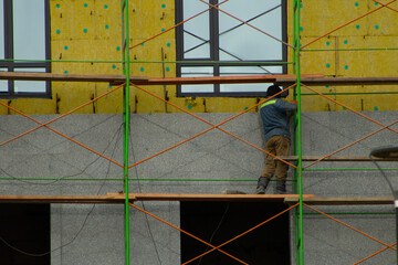 Construction Worker Standing on Scaffolding Applying Cladding to Building Facade