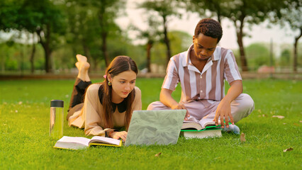 Indian young adult gen z lady female lying on grass use laptop look screen check new email e work garden park. Busy pupil male man do exam study read course book spend break time day college place