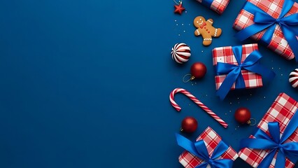 Festive christmas holiday flat lay arrangement of gifts candy canes gingerbread man and ornaments scattered on a deep blue background with copy space for text