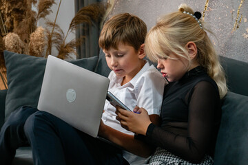 Children Laptop Technology - Two children sit on a couch and use a laptop and tablet.
