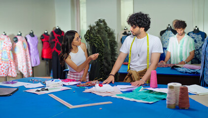 Indian young adult gen z female male man wear tape around neck use tab look screen talk share idea class room place. Tailor girl boy hold pencil do work learn cloth craft create dress pattern on paper