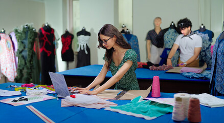 Indian young adult gen z female lady do new day e learning clothe craft skill indoor class room place teen girl wear glasses use laptop look screen typing make fabric pattern on paper work