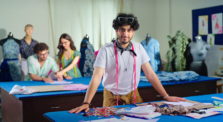 Indian young adult gen z man wear tape around neck learn new craft course look camera class room. Smart teen male boy pupil standing near desk table do casual pose staring cam enjoy day college place