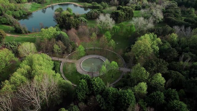 Orbiting drone shot captures an elaborate circular fountain or paved structure surrounded by a pathway, nestled deep within the lush forest of the Parque da Cidade do Porto, Portugal