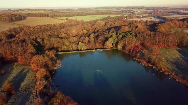 Wide Drone View Tilting Down Of Frozen Pond In Peak District National Park With Ducks And Birds Sat On The Lake In Winter At Golden Hour Sunrise