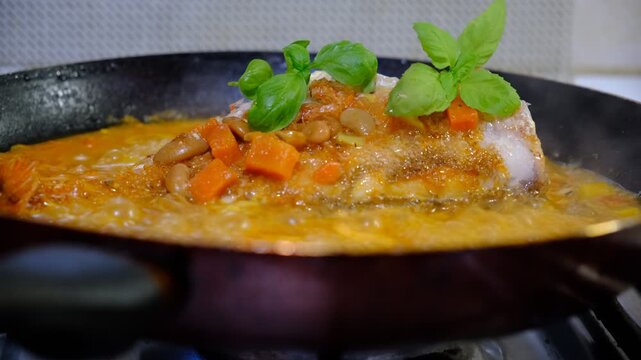 Red sea perch fish with vegetables stew on cooking pan. Cooked with vegetables in samfaina, with tangy tomato caper sauce in a pan. Traditional recipe of Mediterranean gastronomy.
