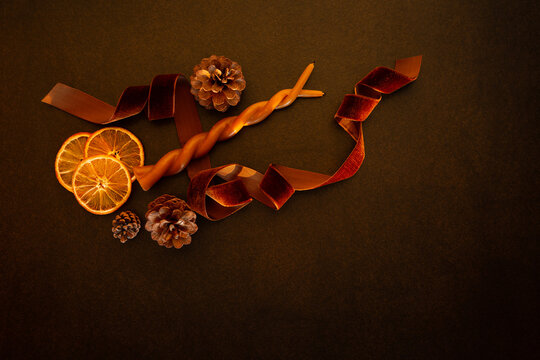 D&eacute;coration naturelle de No&euml;l, tranches d'oranges s&eacute;ch&eacute;es, pommes de pins, bougie orange, ruban velours brun brillant, ensemble pos&eacute; sur un fond brun fonc&eacute;, composition vue du dessus