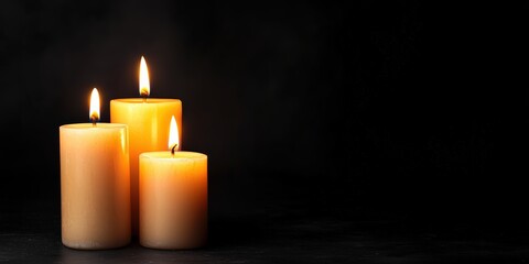 Three glowing pillar candles illuminating a dark background, offering light and spiritual peace with ample copy space