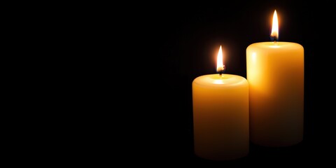 Two lit candles illuminating a dark background, symbolizing remembrance, mourning, and hope with copy space on the left
