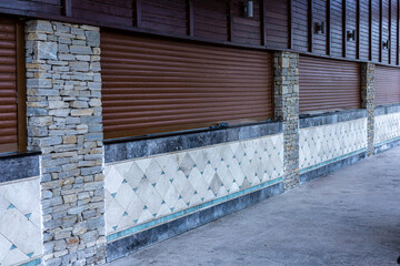 Closed storefront with stone and tile facade. The building features a wooden upper section and metal rolling shutters. ground is concrete and clean.