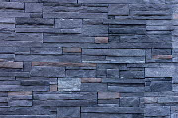 A textured wall made of dark stone bricks arranged in a pattern. The stones vary in size and color, creating a modern and stylish appearance.