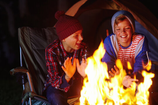 Fire, laughing and night with children camping together for adventure, bonding or survival hobby. Dark, flame and heat with group of funny kids at campsite for holiday, travel or vacation as friends - Powered by Adobe