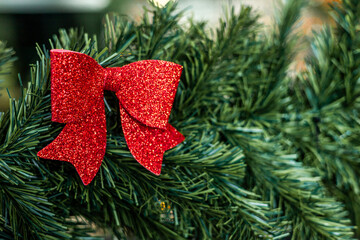 A close-up of a red glitter bow attached to green pine branches. The scene captures festive...